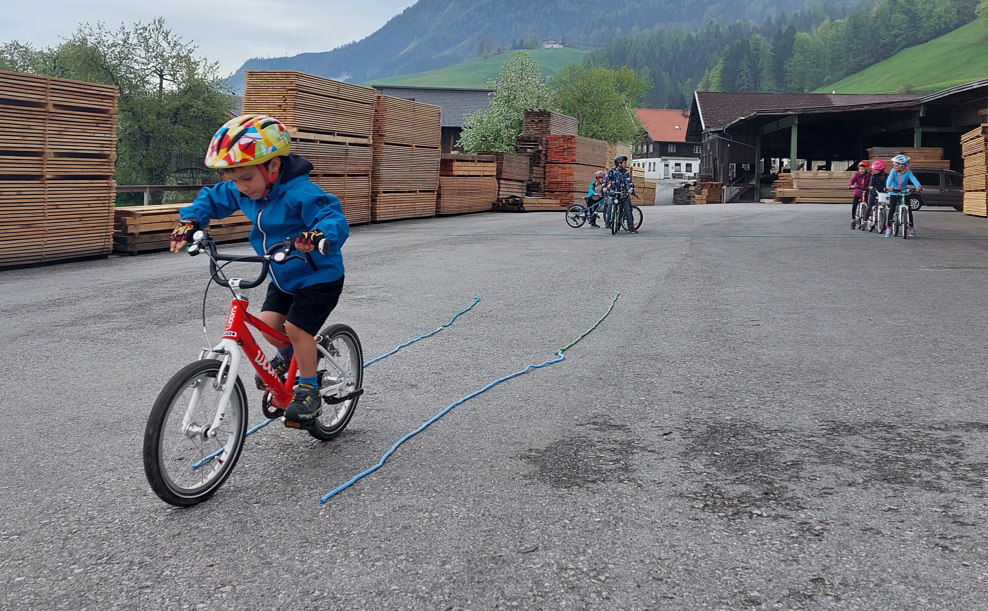 Een kleine jongen rijdt op een woom-fiets rechtdoor tussen twee stukken touw op de grond.