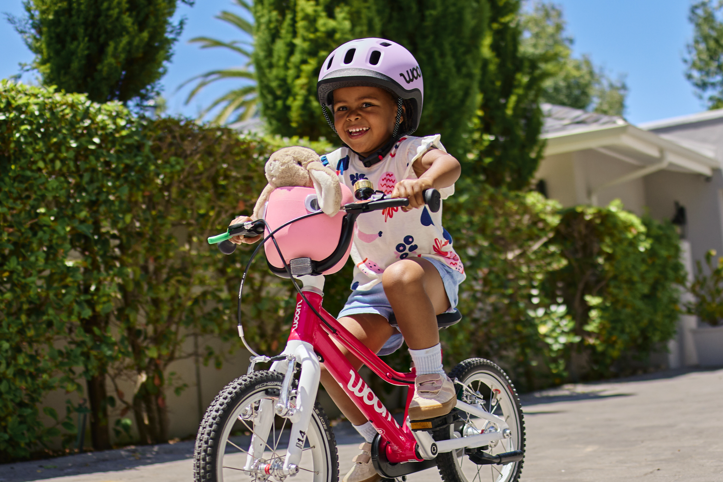 En pige kører på den nye woom 2 med woom cykelkurven i den nye farve marshmallow pink. I kurven sidder et lille krammedyr.